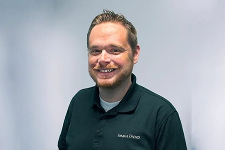 A person with short hair and a beard smiles at the camera. They are wearing a dark polo shirt with "Image Trend" embroidered on it, against a plain background.