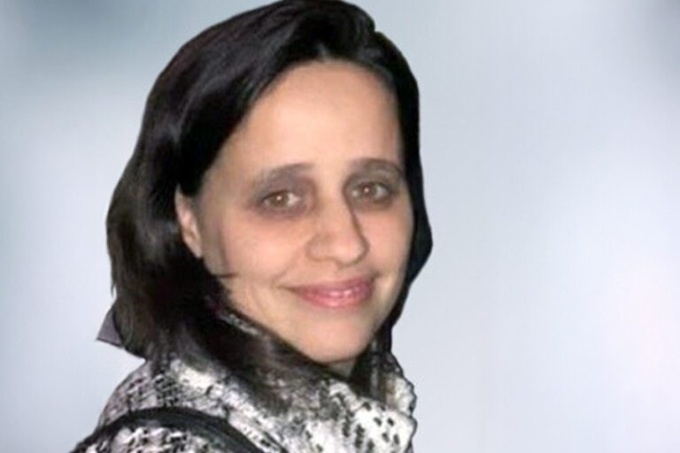 Smiling woman with dark hair wearing a patterned top, against a light background.