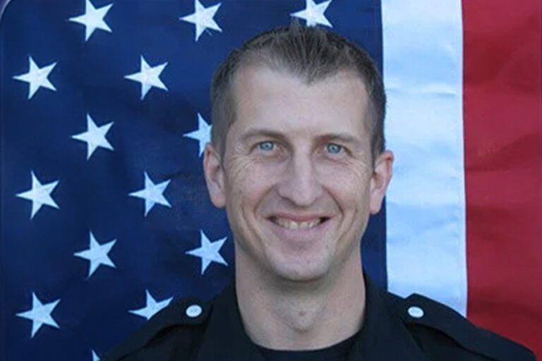 Smiling person in a uniform stands in front of a U.S. flag backdrop.