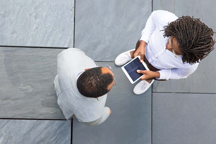 Overhead view of two people on a stone pavement; one in a gray suit, the other holding a tablet.