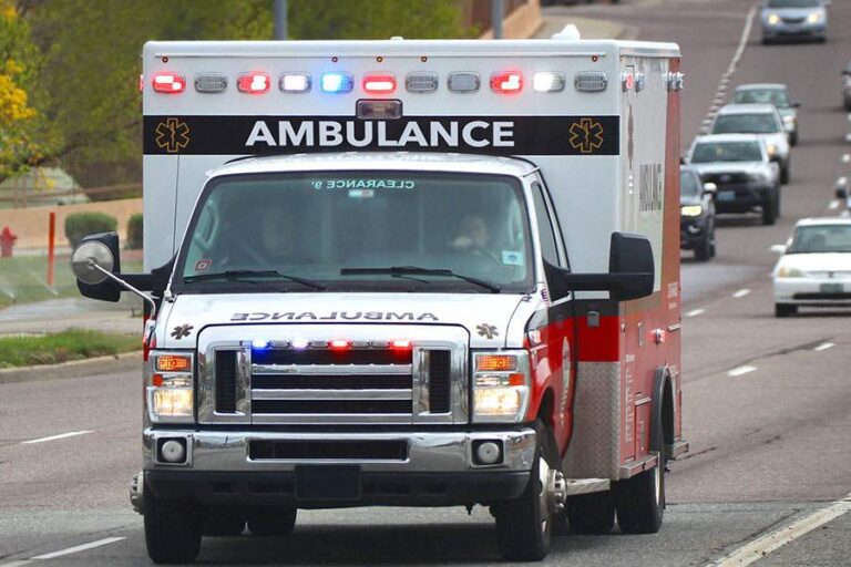front view of ambulance driving down highway with lights on