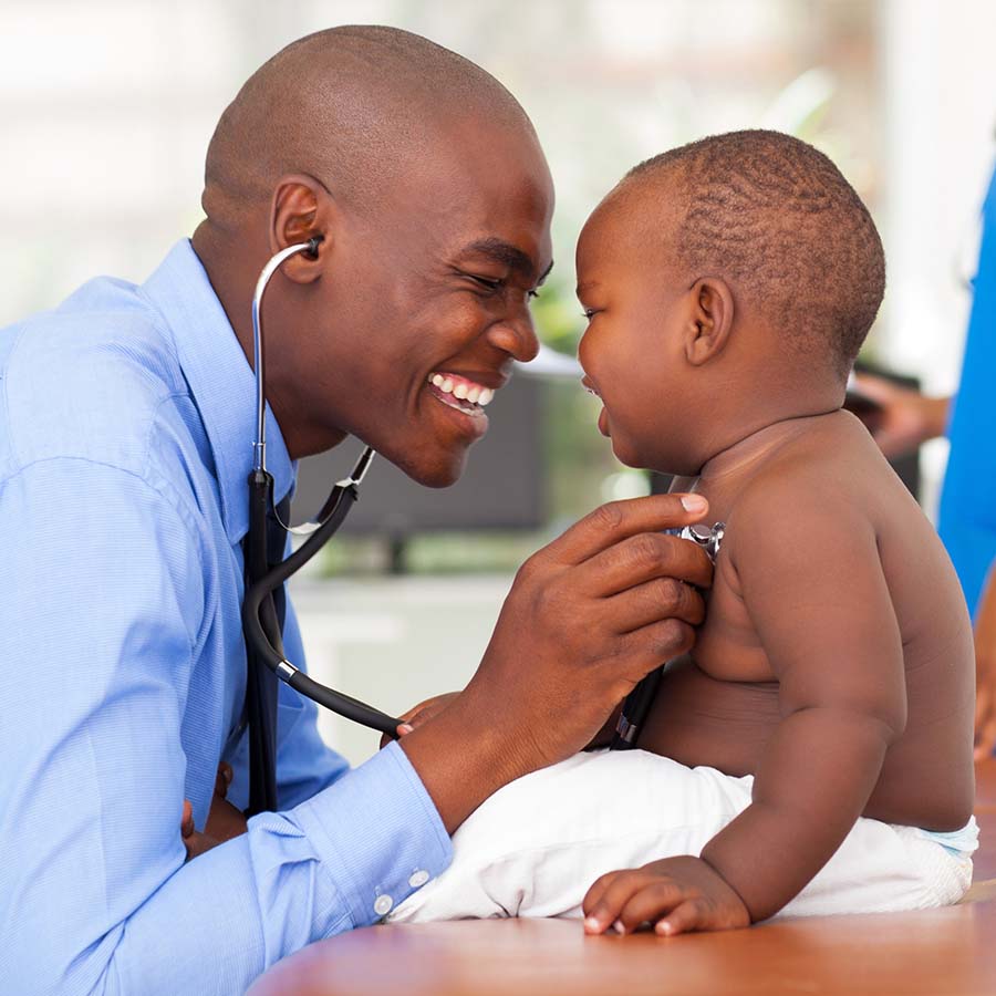 Doctor using a stethoscope to examine a smiling baby sitting on a table.