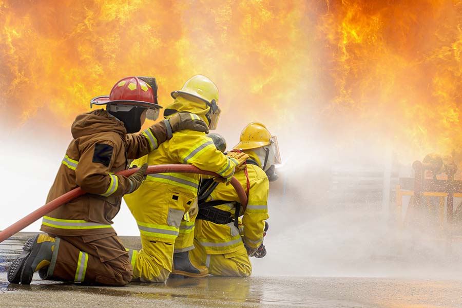 three firefighters kneeling and holding hose that's spraying water on a fire
