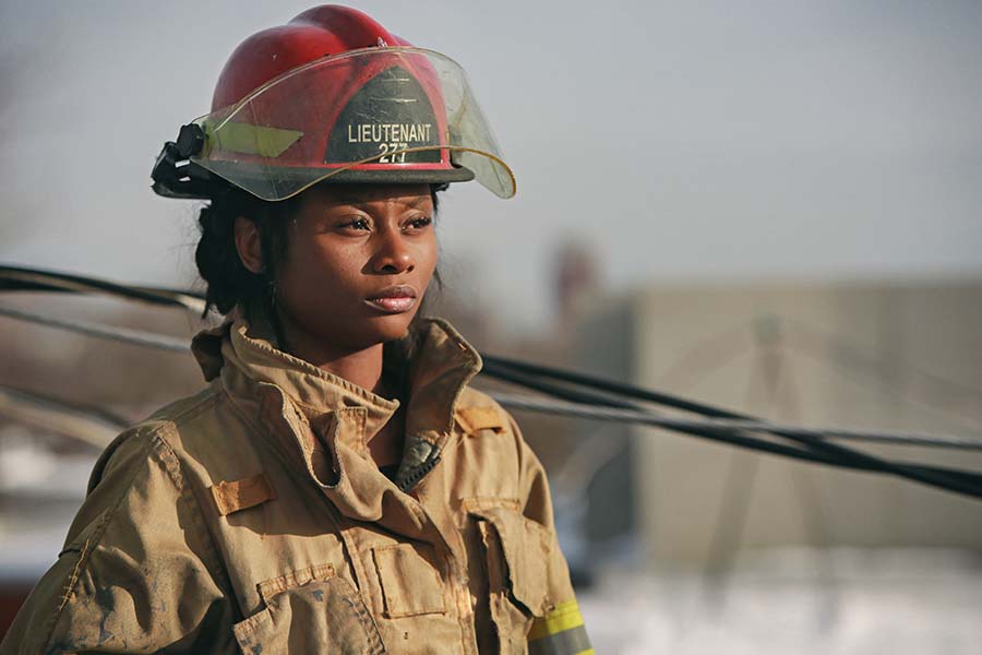 A firefighter in uniform and helmet stands outdoors, gazing into the distance, with a calm expression. "Lieutenant" is visible on the helmet.