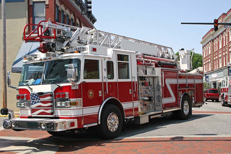 A red and white fire truck with an American flag decal is parked on a street corner surrounded by brick buildings.