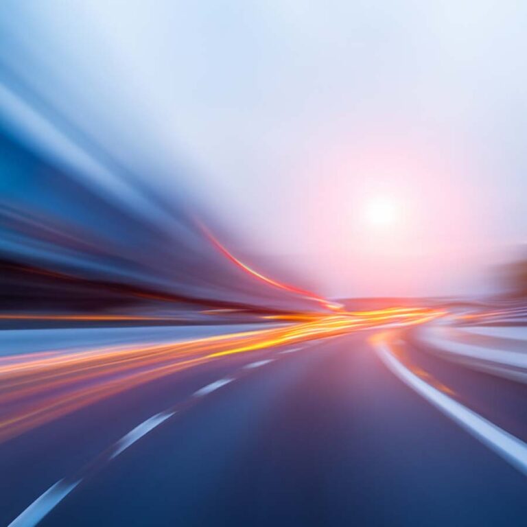 Blurred image of a road with light trails and a glowing sun in the background, creating a sense of speed and motion.