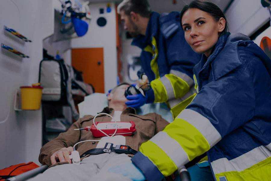 Paramedics assist a patient on a stretcher inside an ambulance, preparing medical equipment for a procedure.