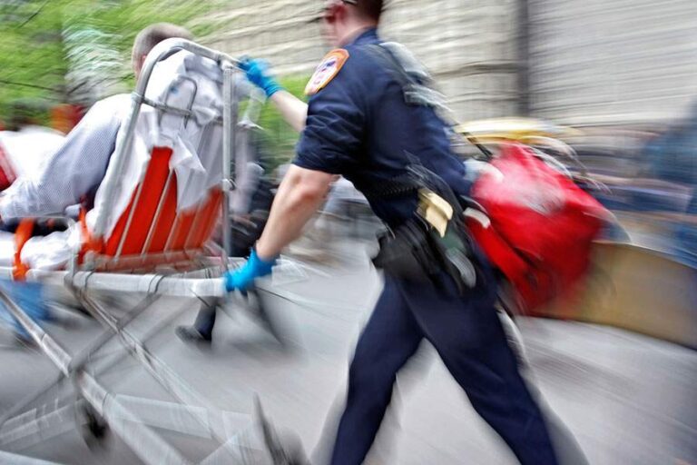 An emergency responder rushes a person on a stretcher through a busy street.