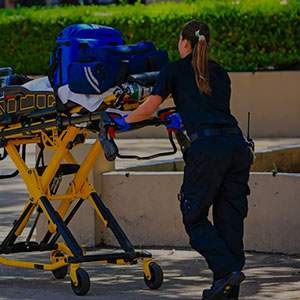 A paramedic pushing a stretcher outdoors, with medical equipment on it.