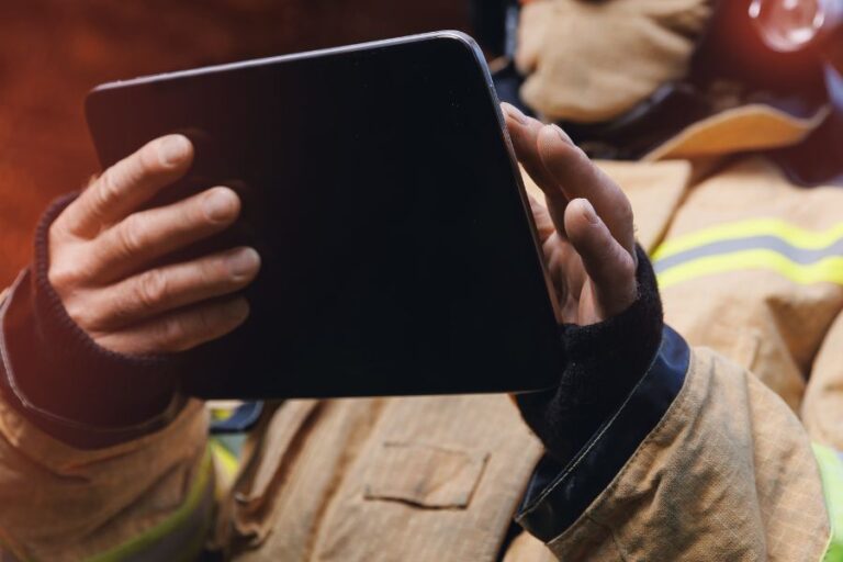 Person in firefighter gear holding a tablet, facing away from the camera.