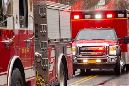 A fire truck and an ambulance with flashing lights are parked on a wet road.