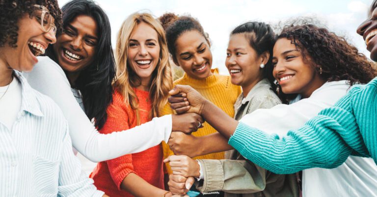 A diverse group of eight people stands together outdoors, smiling and bumping fists, expressing unity and friendship.