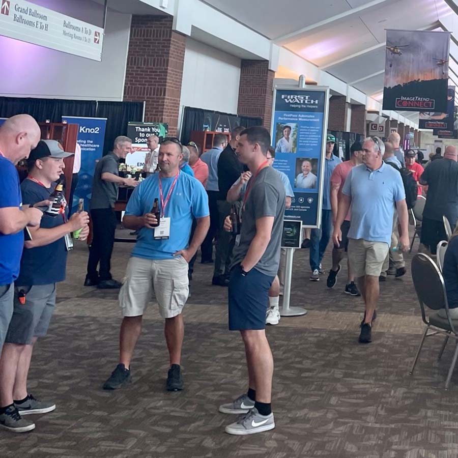People socializing and walking around a trade show or conference venue with displays and banners.