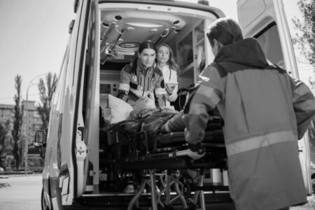 Paramedics load a patient on a stretcher into an ambulance, with medical staff attending and equipment visible inside the vehicle.