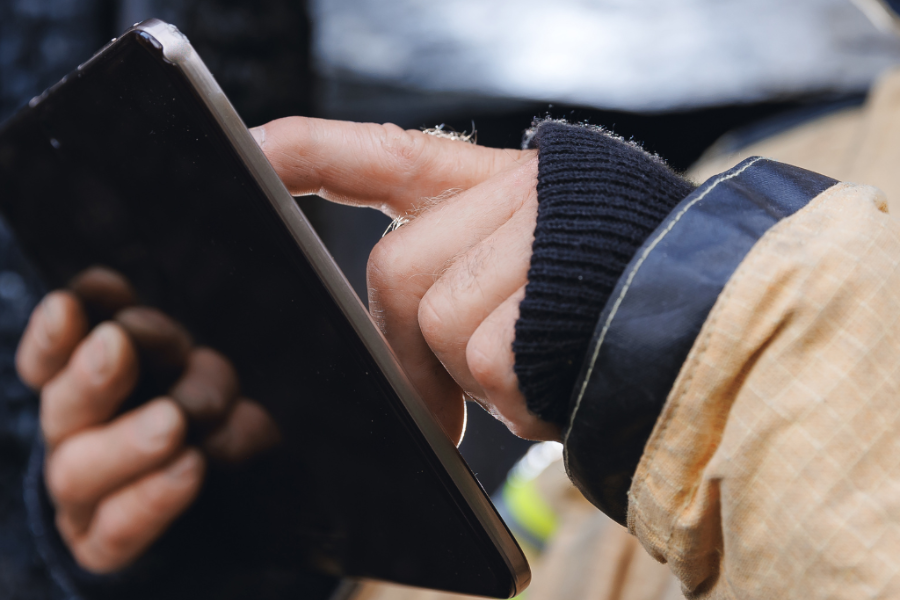 A person wearing a long-sleeve jacket uses their index finger to touch the screen of a black tablet.