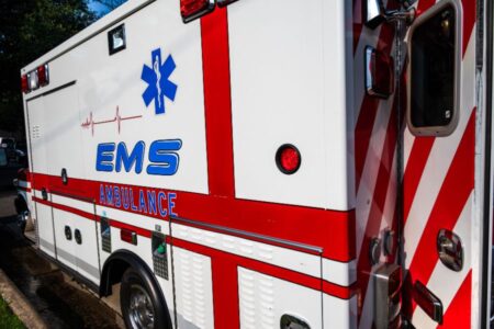 A white EMS ambulance with red stripes and medical symbols is parked on the side of a road.