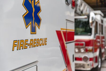 Close-up of a fire-rescue vehicle with another fire truck parked beside it, both featuring emergency markings and symbols.