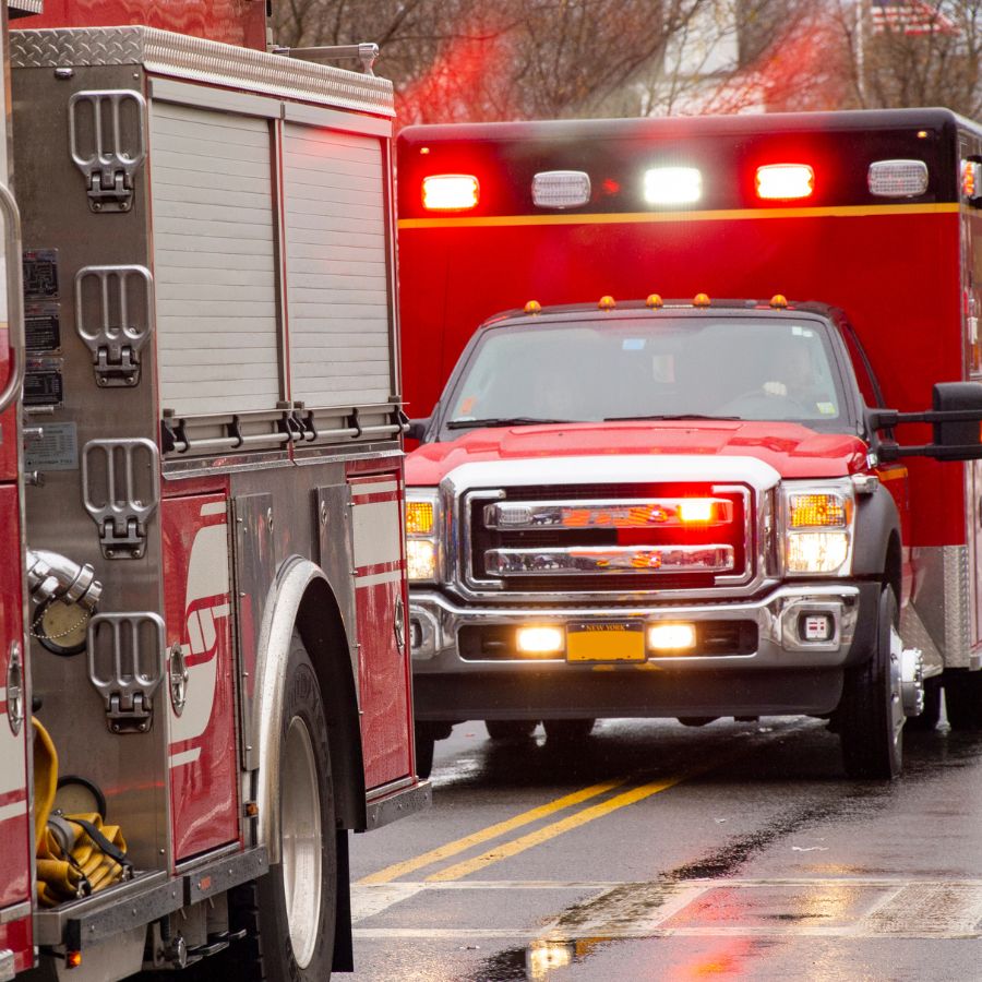 A red fire truck and an ambulance with flashing lights are stopped on a wet road, possibly responding to an emergency.