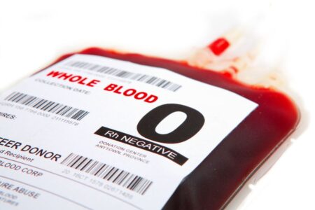 A close-up of a blood donation bag labeled “Whole Blood, O Rh Negative,” with barcodes and donor information visible.