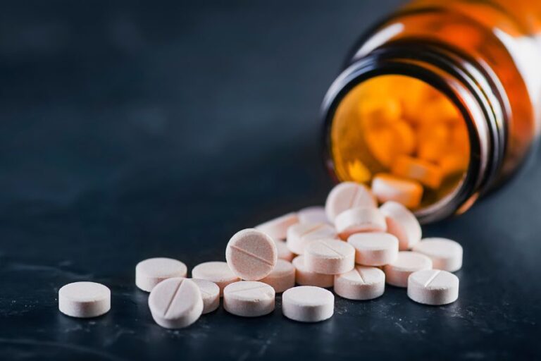 An amber bottle lies on its side with round white tablets spilling out onto a dark surface.