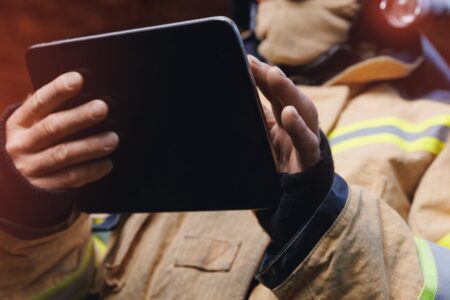 A firefighter in protective gear holds and uses a tablet.