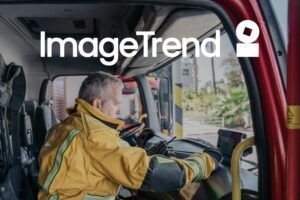 A firefighter in uniform sits inside a fire truck, looking at a device on the dashboard. "ImageTrend" and a logo are overlaid at the top of the image.