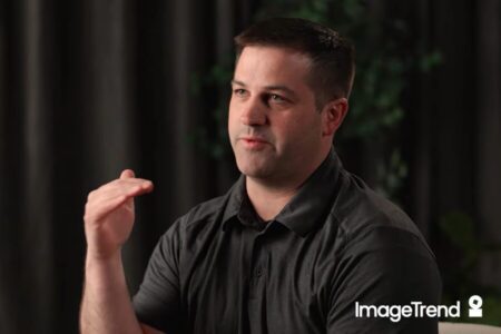 A man in a dark polo shirt gestures with his right hand while speaking, in front of a dark background. The ImageTrend logo appears in the lower right corner, emphasizing the importance of EMS documentation.