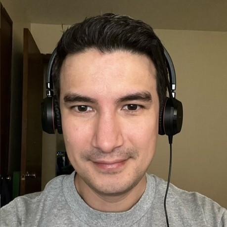 A person wearing a gray shirt and black over-ear headphones faces the camera, indoors, with a neutral expression.
