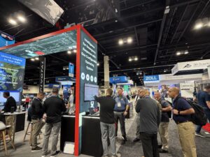 A trade show booth for NERIS medical software featuring a large display screen and people discussing the system.