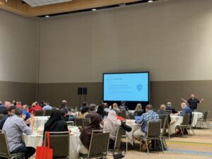 A speaker presents a slide titled “Human In the Loop” for a NERIS conference session in a room full of attendees.