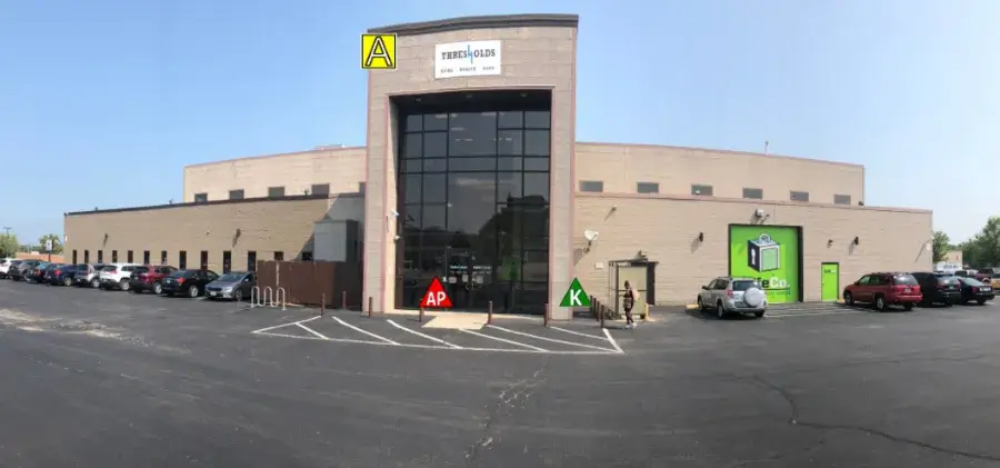 Large industrial building with glass entrance. Numerous cars parked in front. Bright day with clear sky.